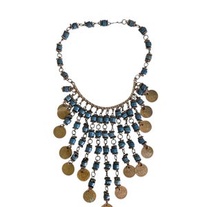 May include: A statement necklace featuring blue beads and dangling gold-colored coin charms. The necklace has a circular design with multiple strands of beads and coins, creating a layered effect. The necklace is set against a white background.