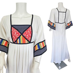 Könnte beinhalten: Ein weißes Maxikleid mit Patchwork-Design am Oberteil und bunten Streifenbesatz an den Ärmeln. Das Kleid hat einen quadratischen Ausschnitt und einen gerafften Rock.