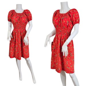 May include: Red floral print dress with a smocked bodice and short sleeves. The dress features a round neckline and pockets. The fabric is covered in small yellow and brown floral patterns. The dress is displayed on a mannequin.