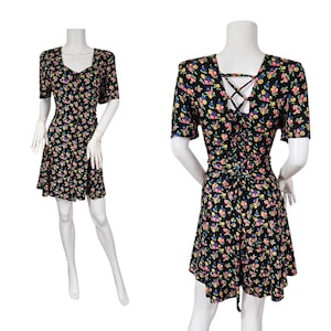 May include: Black floral print dress with a V-neck and short sleeves. The dress features a fitted waist and a flared skirt. The back of the dress has a criss-cross lace-up detail. The dress is adorned with small pink, yellow, and blue flowers.