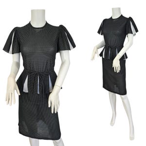Puede incluir: Vestido negro con lunares blancos, cintura peplum y mangas cortas. El vestido tiene un cinturón a juego y una falda hasta la rodilla. Las mangas tienen detalles blancos. El vestido se exhibe en un maniquí.