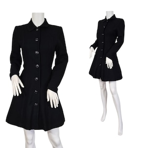 Puede incluir: Un abrigo de lana negro con botones y falda acampanada. El abrigo tiene mangas largas y un cuello clásico. El abrigo se exhibe en un maniquí. El abrigo es de estilo clásico.