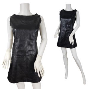 May include: A black sleeveless dress made of faux leather. The dress has a boat neckline and a slightly flared skirt. The dress is displayed on a mannequin. The dress has a seam down the front and back.