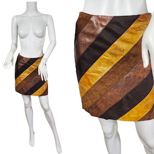 May include: A mini skirt with diagonal stripes in shades of brown, black, and yellow. The skirt is made of leather and has a patchwork design. The skirt is displayed on a mannequin.