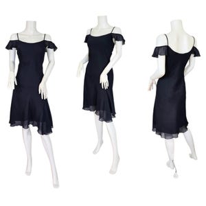 May include: A navy blue dress with spaghetti straps and off-the-shoulder ruffles. The dress has a flared skirt with a sheer, ruffled hem. The dress is displayed on a mannequin, showcasing the design from multiple angles.