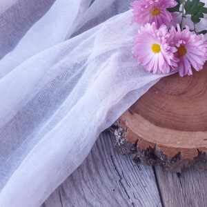 Puede incluir: Flores rosas sobre una rodaja de madera con una tela blanca transparente drapeada sobre ella.