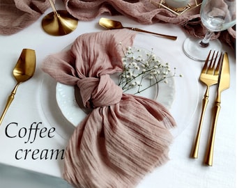 May include: A dining table set with a coffee cream coloured runner and napkin. Gold-coloured cutlery, a candle holder, and a geometric terrarium are arranged on a white tablecloth. A white vase holds white flowers.
