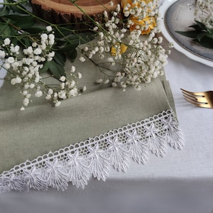 May include: A green linen napkin with white lace trim, a white candle with a burlap ribbon, a small Eiffel Tower figurine, and white baby's breath flowers on a wooden slice.