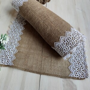 Peut inclure: Un chemin de table en toile de jute brune avec une bordure en dentelle blanche. Le chemin de table est roul&eacute; et la bordure en dentelle est visible aux deux extr&eacute;mit&eacute;s.