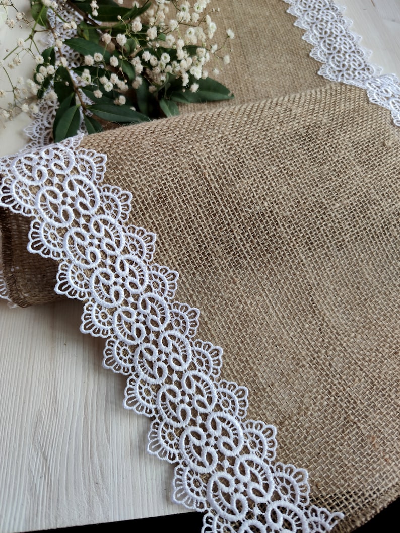 Peut inclure: Un chemin de table en toile de jute avec une bordure en dentelle blanche. Le chemin de table est pli&eacute; en deux et la bordure en dentelle est visible des deux c&ocirc;t&eacute;s.