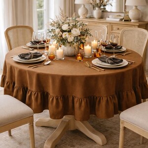 a beautifully set dining table with a brown tablecloth, a vase of flowers, and candles. The table is set with plates, silverware, and glasses, creating an inviting and elegant atmosphere.