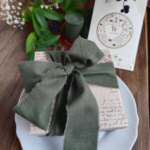 May include: A gift wrapped in brown paper with a green ribbon tied in a bow. The paper is covered in handwritten text. The gift is sitting on a white plate.