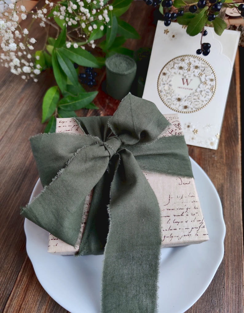 May include: A gift wrapped in brown paper with a green ribbon tied in a bow. The paper is covered in handwritten text. The gift is sitting on a white plate.