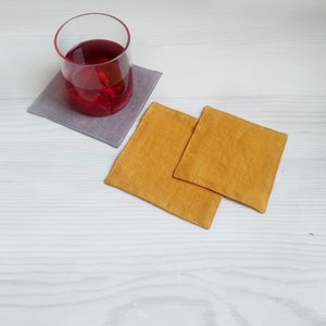 Pode incluir: Dois  tapetes quadrados de tecido, um cinza e outro amarelo, com um copo de líquido vermelho sobre o tapete cinza.