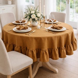 a beautifully set dining table with a yellow tablecloth, white plates, and gold cutlery. The table is set for four people, with a vase of flowers and candles as the centerpiece. The table is surrounded by four chairs, and the overall color scheme is warm and inviting.