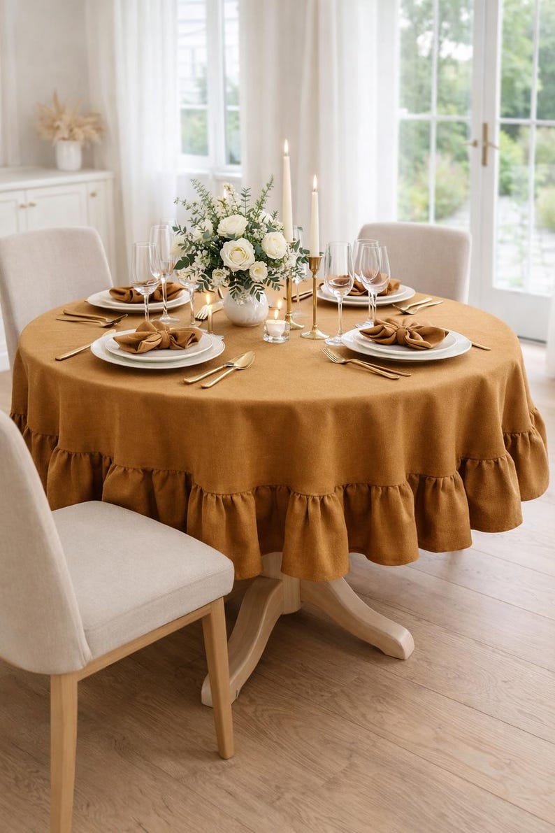 a beautifully set dining table with a yellow tablecloth, white plates, and gold cutlery. The table is set for four people, with a vase of flowers and candles as the centerpiece. The table is surrounded by four chairs, and the overall color scheme is warm and inviting.