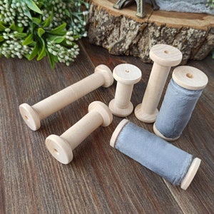 May include: Six wooden spools with gray velvet ribbon wound around them. The spools are on a wooden surface.