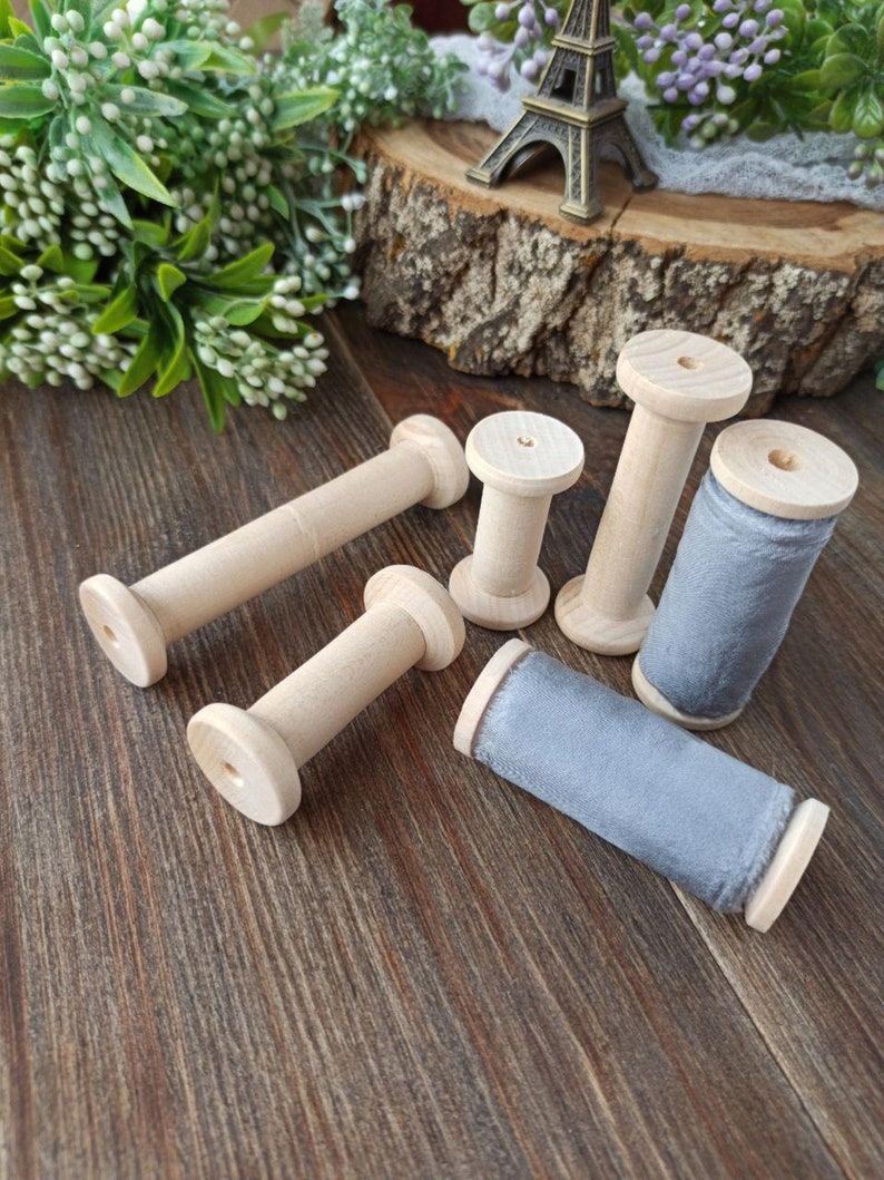 May include: Six wooden spools with gray velvet ribbon wound around them. The spools are on a wooden surface.