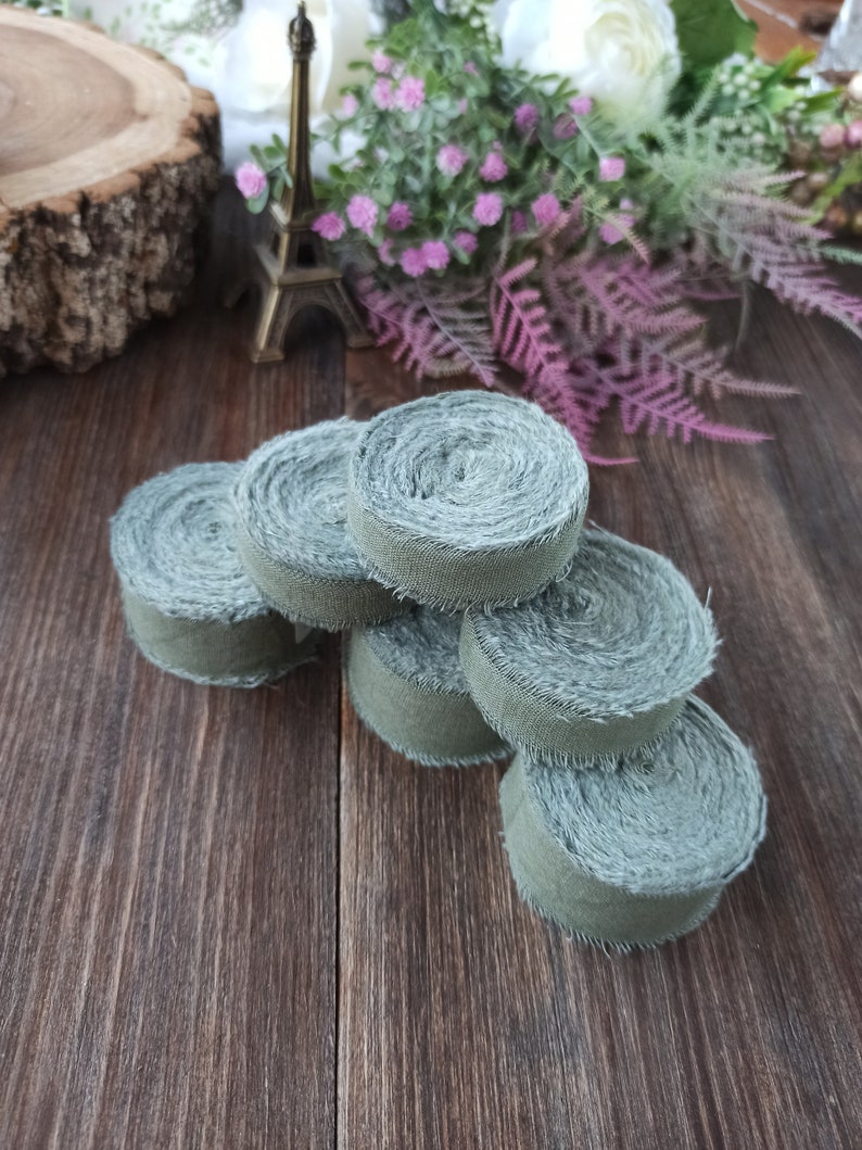 May include: A stack of six green fabric ribbon rolls, each with a frayed edge. The rolls are arranged in a pyramid shape on a wooden surface.
