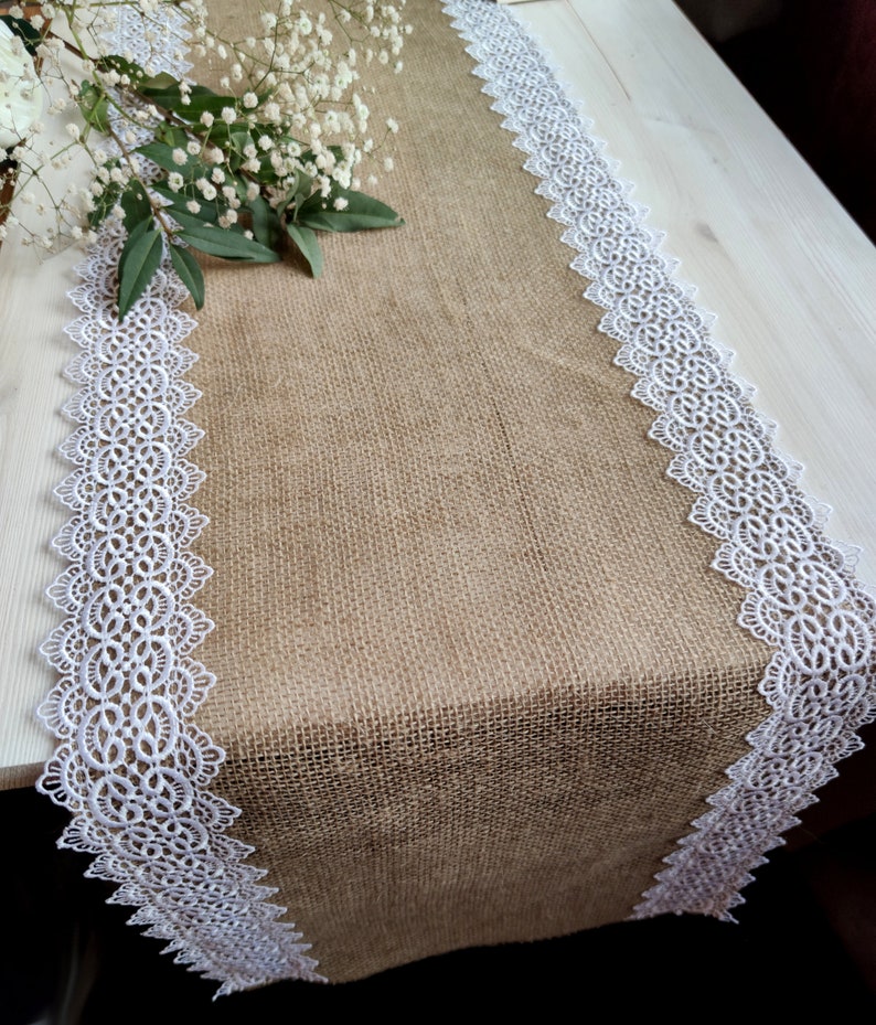 Peut inclure: Un chemin de table en toile de jute brune avec une bordure en dentelle blanche. Le chemin de table est sur une table en bois clair.