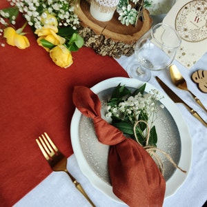 May include: A rustic table setting with a white candle, a small Eiffel Tower, and a white plate with a brown napkin tied in a knot. The napkin is on a gray plate with a white rim. A gold fork and knife are on the table.