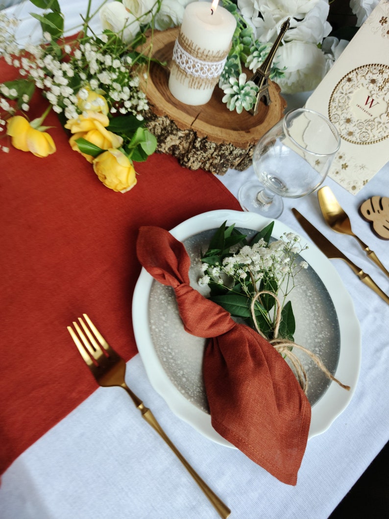 May include: A rustic table setting with a white candle, a small Eiffel Tower, and a white plate with a brown napkin tied in a knot. The napkin is on a gray plate with a white rim. A gold fork and knife are on the table.