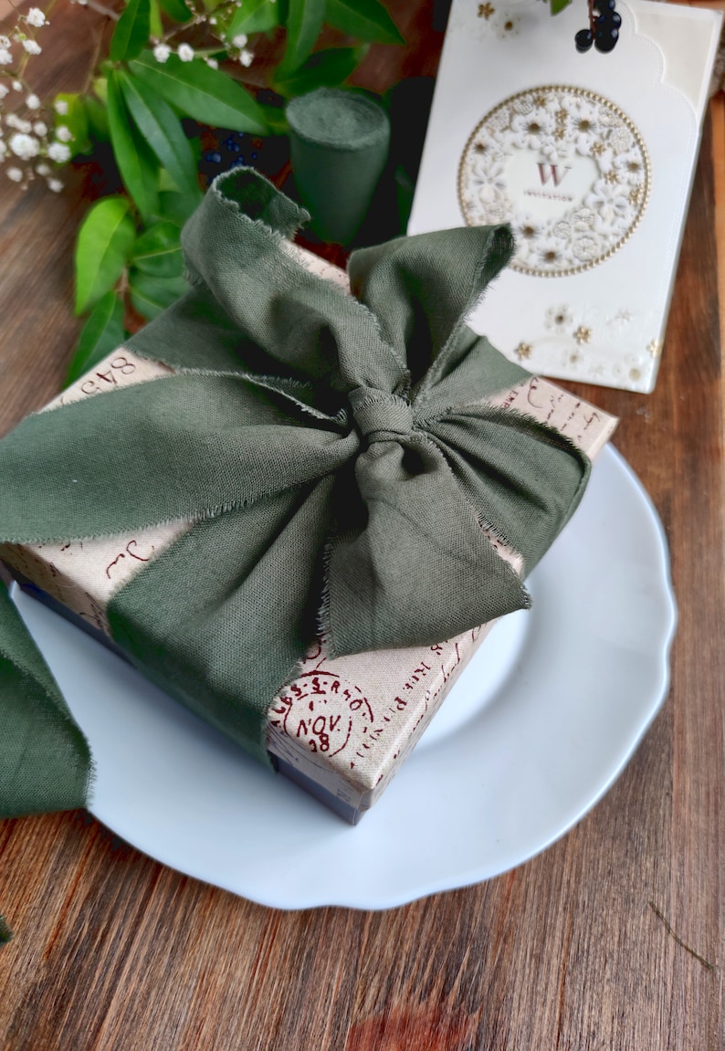May include: A gift box wrapped in brown paper with a green fabric ribbon tied in a bow. The box has red stamps and handwritten text on it. The box is sitting on a white plate.