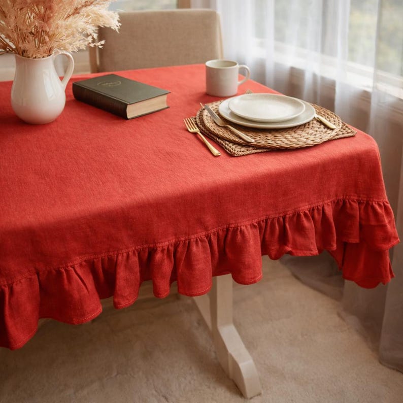 a table set with a red tablecloth, plates, a book, and a vase of dried flowers.