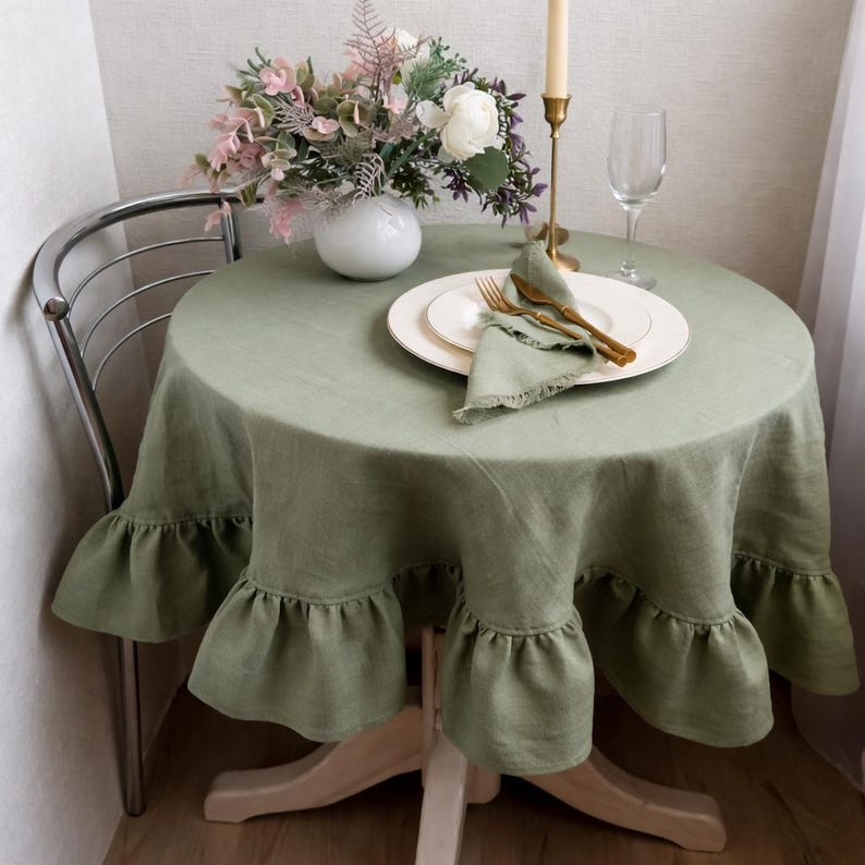 a table set for a meal, with a white plate, a green tablecloth, and a vase of flowers. The table is surrounded by a chair, and there is a candle and a wine glass on the table.