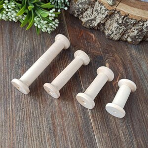 May include: Four wooden spools of different sizes, all in a natural wood color. The spools are arranged on a wooden surface.