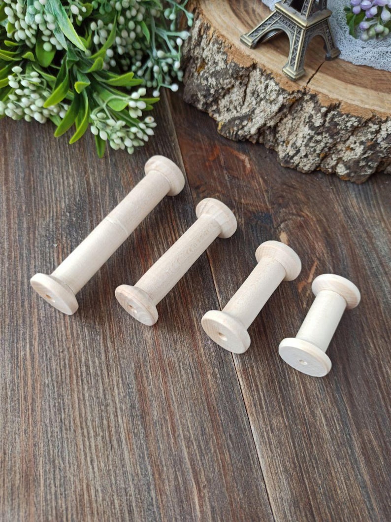 May include: Four wooden spools of different sizes, all in a natural wood color. The spools are arranged on a wooden surface.