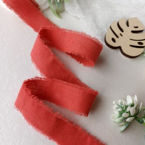 May include: A coral red ribbon with frayed edges. The ribbon is made of a soft, textured fabric and is perfect for adding a touch of color and texture to your crafts.