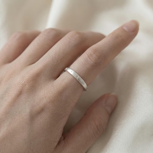 May include: A silver ring with a band featuring small star-shaped engravings. The ring is worn on a finger, showcasing its simple yet elegant design. The ring's surface reflects light, highlighting its polished finish.