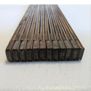 Puede incluir: Una regla plegable de madera vintage con bordes metálicos. La regla está cerrada y muestra los bordes metálicos de cada sección.