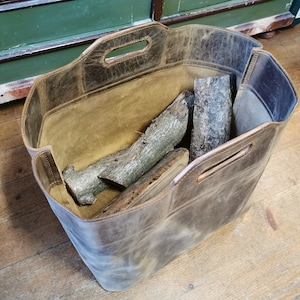 Könnte beinhalten: Ein brauner Leder-Holzkorb mit Griff, gefüllt mit Brennholz.