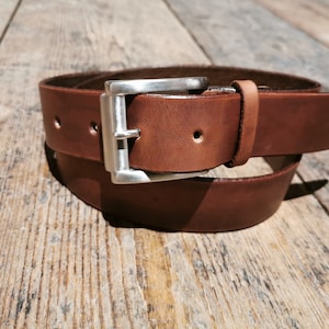 May include: A brown leather belt with a silver buckle. The belt is folded in half and the buckle is in the centre of the image.