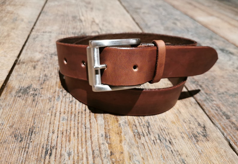 May include: A brown leather belt with a silver buckle. The belt is folded in half and the buckle is in the centre of the image.