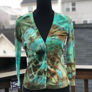 May include: A tie-dye cardigan in shades of teal, brown, and green. The cardigan has a v-neck and long sleeves. It is made of a soft, lightweight fabric.
