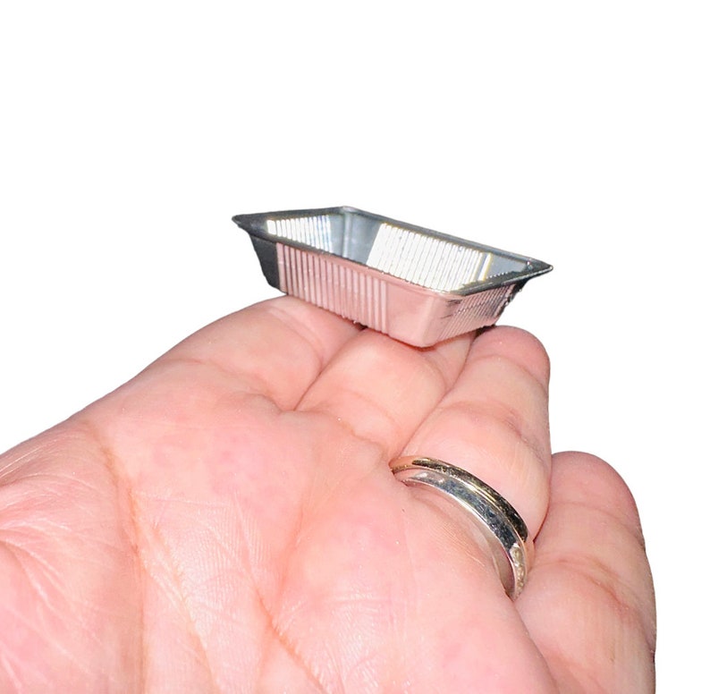 May include: A small, rectangular, silver-coloured aluminium foil baking pan with a ribbed exterior. The pan is empty and appears unused. The pan is held in a person's hand.