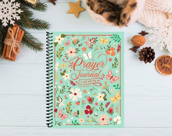 May include: A teal blue prayer journal with a floral and butterfly design. The cover reads "Prayer Journal" and "It is well with my soul!" with the words "For Women" below. The journal is spiral bound and made in the USA.