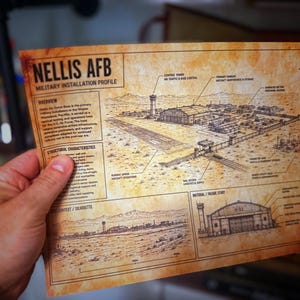 May include: A rectangular paper print with a sepia-toned, aged appearance featuring a military installation profile of Nellis AFB. The document includes detailed line drawings of the airfield, hangars, and control tower, along with technical text labels.