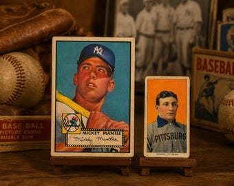 May include: Vintage baseball cards featuring Mickey Mantle and a Pittsburg player. The Mantle card shows him in a Yankees uniform. A baseball glove and ball are visible, along with a vintage baseball card box.