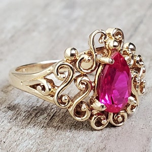 Peut inclure: Une bague en or avec une pierre précieuse rose en forme de poire sertie dans un délicat motif de filigrane.
