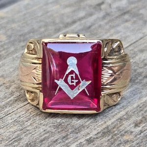 May include: A gold ring with a red stone and a white Masonic symbol engraved on the stone.