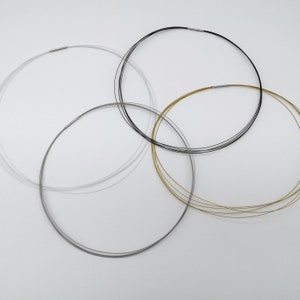 Op de afbeelding: Vier verschillende gekleurde metalen kettingen, een zilveren, een gouden, een zwarte en een witte, liggen op een wit oppervlak.