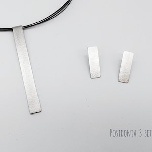 Puede incluir: Un collar de plata con un colgante rectangular largo y pendientes rectangulares de plata a juego. El conjunto está etiquetado como "POSIDONIA S SET".