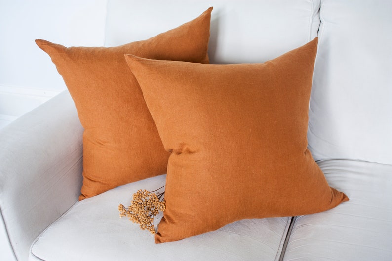 May include: Two burnt orange linen throw pillows on a white sofa.