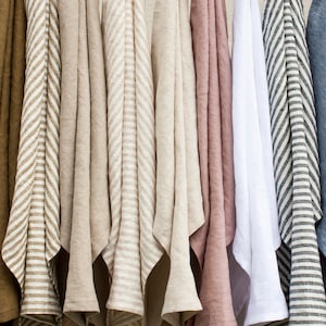 Pu&ograve; includere: Una collezione di tessuti di lino in vari colori, tra cui ruggine, verde oliva, beige, rosa, bianco e blu. Alcuni tessuti presentano motivi a righe. I tessuti sono appesi, mostrando la loro consistenza e drappeggio.