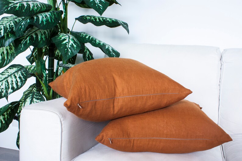 May include: Two brown linen throw pillows with a zip closure on a white sofa.