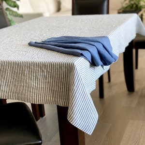 May include: A white linen tablecloth with blue stripes, folded in half and placed on a wooden table. A blue linen napkin is folded on top of the tablecloth.